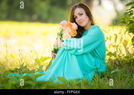 Ritratto di una giovane ragazza con un mazzo di rose seduti all'ombra degli alberi in una giornata di sole Foto Stock