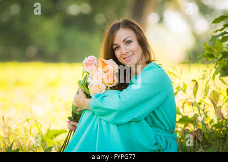 Ritratto di una giovane ragazza con un mazzo di rose seduti all'ombra degli alberi in una giornata di sole Foto Stock