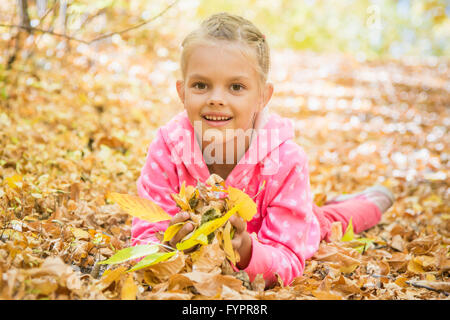 6 anno vecchia ragazza giacente sul giallo caduta foglie Foto Stock