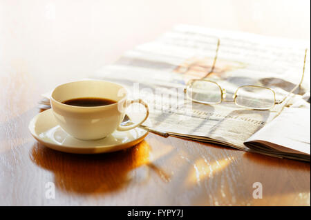Tazza di caffè, con i giornali e i bicchieri, su una luminosa mattina di sole. Foto Stock