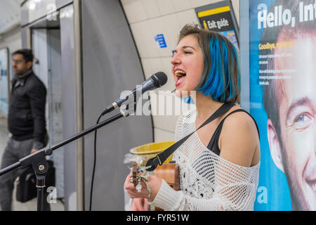 Jazz Mino canta e suona l'ukulele come ella busks per passeggeri in transito attraverso la Waterloo Stazione della metropolitana di Londra. Ella è Foto Stock