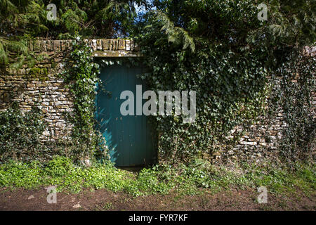 Un dipinto di verde di porte in legno nascosta in un lungo muro di pietra. Foto Stock