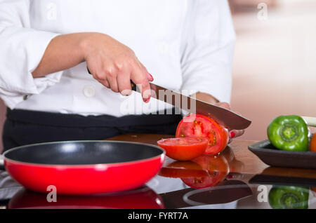 Closeup chef pomodoro di taglio su una superficie di legno con padella rossa nella parte anteriore Foto Stock