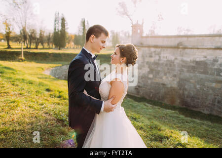 Sposa e lo sposo sul prato verde di guardare tutti gli altri bracci di trattenimento. Al tramonto Foto Stock