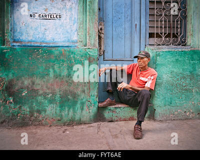 Un uomo si siede su una porta in prossimità di un cartello che diceva, "Post le fatture non' in spagnolo. L'edificio sembra abbandonata ma egli può ben essere seduta in attesa per il proprietario. Foto Stock