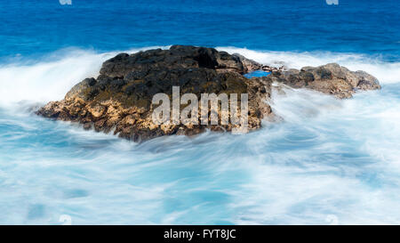 Lunga durata shot di onde che scorre sulla roccia di lava Foto Stock