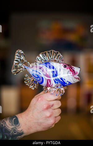 Un uomo detiene una scultura di vetro di un pesce in mano a un vetro soffiando studio sulla Whidbey Island, WA. Foto Stock