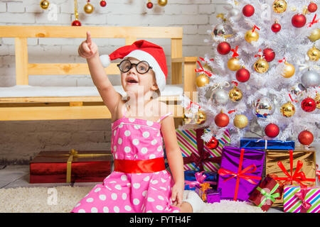 La ragazza di Red Hat e le divertenti bicchieri arrotondati punti il dito su qualcosa di interessante Foto Stock