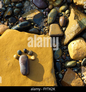 Lonely piede da pebble su sfondo di roccia, sorprendente concetto sulla superficie di pietra con il colore giallo, arte prodotto al mare Foto Stock