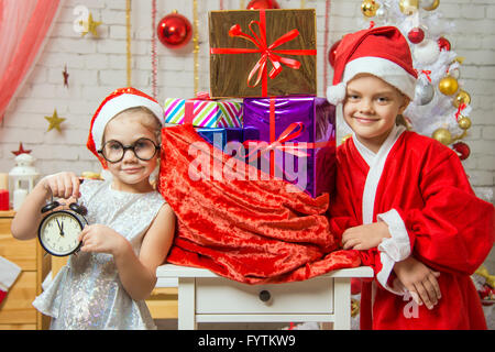 Ragazza mostra sull'orologio, una ragazza vestita come Santa Claus è in piedi presso la borsa con doni Foto Stock
