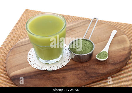 Erba di frumento health drink con polvere nel convogliatore e cucchiaio su di un legno di acero scheda sopra il bambù e sfondo bianco. Foto Stock