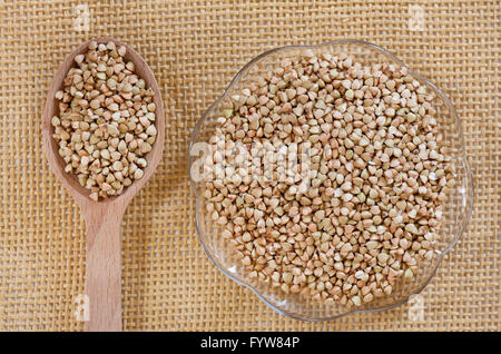 Bianco di semole e semolini di grano saraceno giacente su vetro piattino e cucchiaio di legno sul tappetino, materie non prodotto arrosto cibo sano e porzione di cucitura. Foto Stock