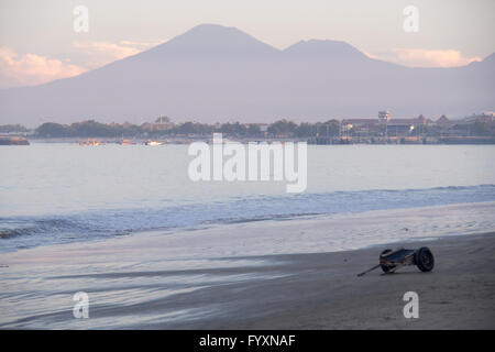 Un rimorchio in legno per il lancio di imbarcazioni nella baia di Jimbaran, Bali, nelle prime ore del mattino e le montagne in distanza. Foto Stock