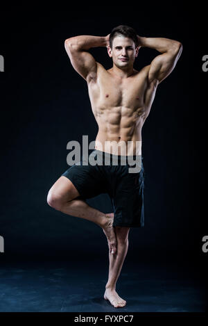 Uomo muscolare in equilibrio su una gamba rilassati sfondo scuro Foto Stock