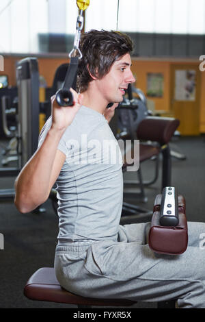 Giovane uomo che esercitano nel centro fitness su un pull-up macchina Foto Stock