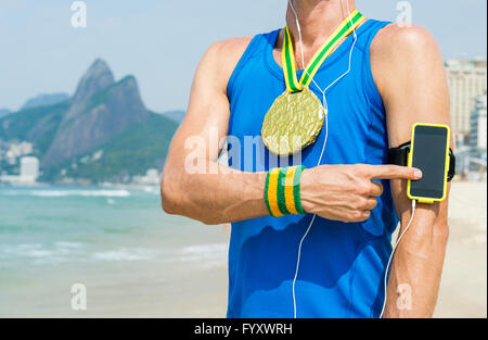 Medaglia d'oro atleta che indossa telefono cellulare touchscreen technology armband sta ascoltando musica motivazionale sulla spiaggia di Ipanema Foto Stock