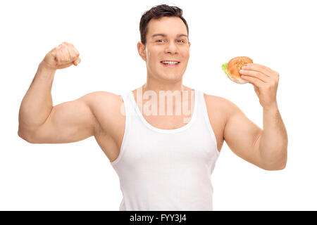 Giovane uomo flettendo il suo bicipite e tenendo un sandwich in altro canto isolato su sfondo bianco Foto Stock