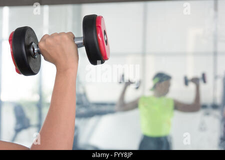 Un giovane uomo orologi muscolo del braccio in piedi di fronte a uno specchio come egli esegue un bicipite curl con un manubrio cromato Foto Stock