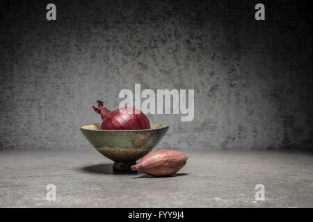 Alimentare la vita ancora con la cipolla rossa in un recipiente e lo scalogno sul tavolo di pietra nella cucina moderna. Foto Stock