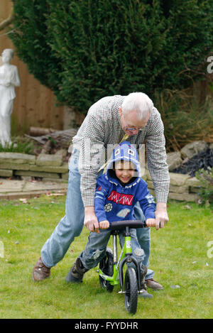 Un nonno aiutando il suo nipote (3 anni) per imparare ad andare in bicicletta Foto Stock