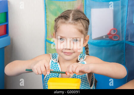 Felice bambina di cinque anni affina un temperamatite piccolo Foto Stock