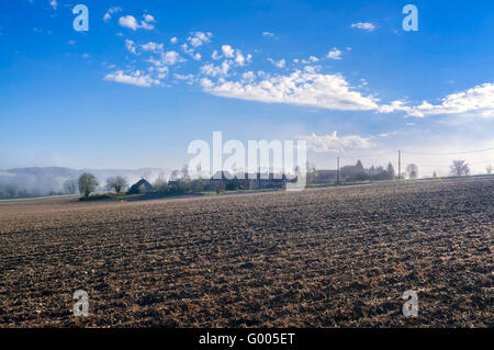 Early Morning mist attraverso campo arato e village - Francia. Foto Stock