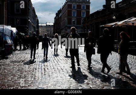 La gente camminare gettando ombre su strade acciottolate intorno al Covent Garden di Londra su bagnato pomeriggio REGNO UNITO Foto Stock