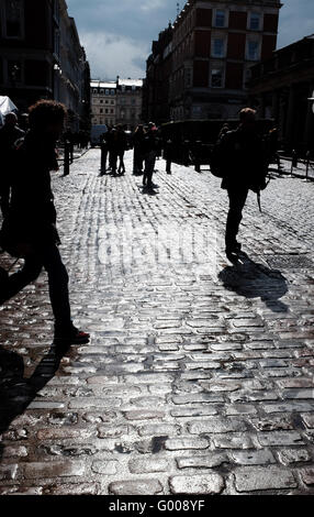 La gente camminare gettando ombre su strade acciottolate intorno al Covent Garden di Londra su bagnato pomeriggio REGNO UNITO Foto Stock