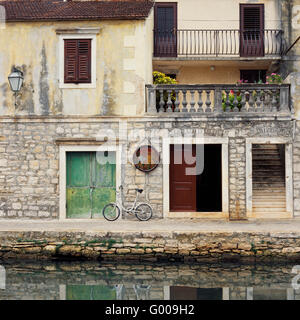 Case in pietra e negozi linea un canale nel villaggio storico di Vrboska, Isola di Hvar, Croazia. Una bicicletta si appoggia contro una parete. Foto Stock