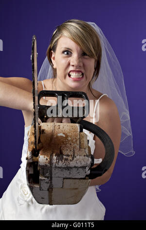 Arrabbiato giovane sposa con un chainsaw su uno sfondo blu scuro Foto Stock