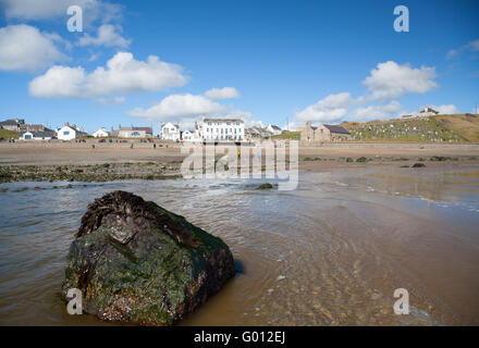 La vista verso Aberdaron village (mostra pub & chiesa) presi dalla spiaggia con la bassa marea su un estate giornata di primavera con il blu del cielo Foto Stock