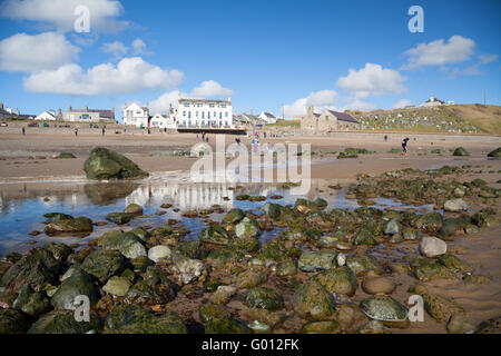 La vista verso Aberdaron village (mostra pub & chiesa) presi dalla spiaggia con la bassa marea su un estate giornata di primavera con il blu del cielo Foto Stock