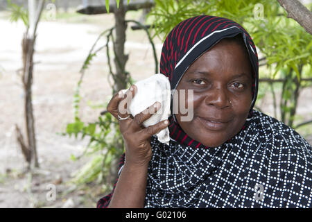 Una vecchia donna tenendo una conchiglia per l'orecchio per ascoltare i suoni del mare m Foto Stock