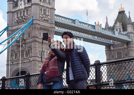 Turisti asiatici tenendo selfie con il Tower Bridge in background, Londra England Regno Unito Regno Unito Foto Stock