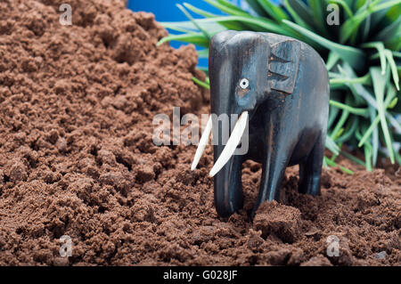 In legno elefante africano intagliare sulla sabbia con pianta verde e blue sky in background Foto Stock