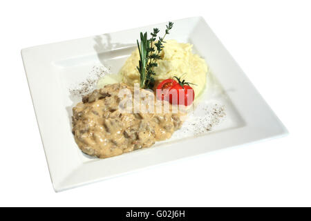 Un manzo stroganoff pasto con purè di patate e pomodoro. Decorate con timo e rosmarino. Isolato su bianco Foto Stock