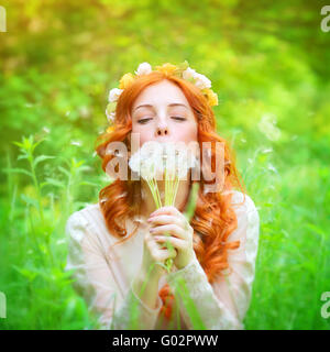 Closeup ritratto di una bellissima femmina sognante tenendo in mano i fiori di tarassaco e con gli occhi chiusi soffiando su di esso Foto Stock