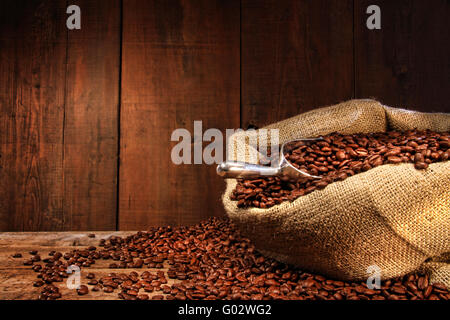 Sacco di tela di chicchi di caffè contro il legno scuro Foto Stock