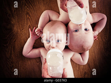 Baby gemelli di bere latte dalla bottiglia tenendo da parte dei loro genitori Foto Stock