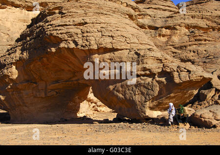 Bedouin uomini seduti su un arco di roccia, il deserto del Sahara Foto Stock