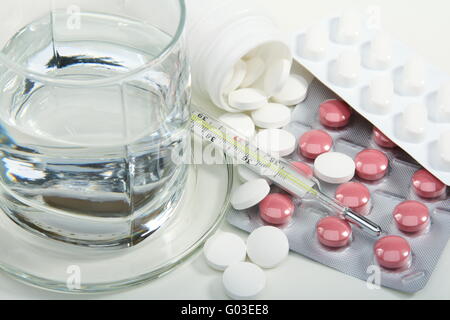 Diverse le pillole, bicchiere di acqua e termometro medico. Foto Stock