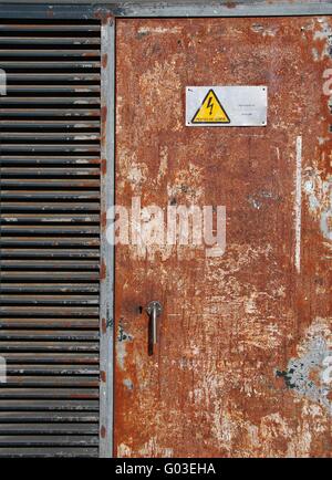 Pericolo alta tensione segno su un metallo arrugginito porta Foto Stock