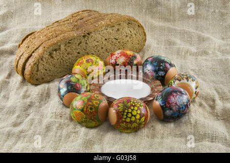 Molti freschi rurale di pasqua uova decorate giacenti in un wattled Piccolo cesto vicino al pane fresco e saltcellar su un panno da un roug Foto Stock