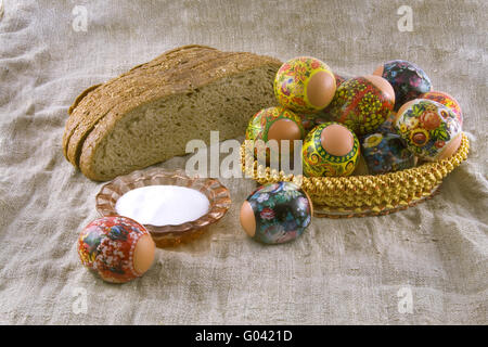 Molti freschi rurale di pasqua uova decorate giacenti in un wattled Piccolo cesto vicino al pane fresco e saltcellar su un panno da un roug Foto Stock