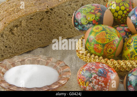 Molti freschi rurale di pasqua uova decorate giacenti in un wattled Piccolo cesto vicino al pane fresco e saltcellar su un panno da un roug Foto Stock