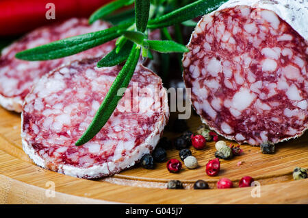 Close up salame peper calli rosmarino sul bordo di taglio Foto Stock