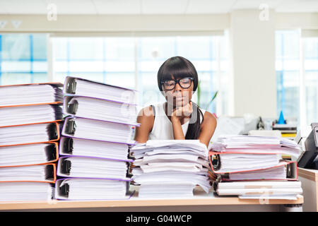 Triste afro american imprenditrice di sedere a tavola con molti lavori in ufficio Foto Stock