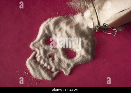 Lo zucchero bianco di fuoriuscita del vasetto di vetro su sfondo rosa e formando una faccia del cranio Foto Stock