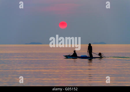 La barca con i pescatori in mare su uno sfondo di tramonto Foto Stock