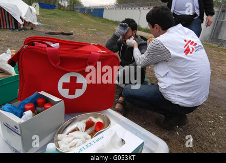 Il Dottor Vladimir Andric, MSF il Capo della Clinica Mobile, considera un rifugiato ferito in faccia. In retro-massa la parete e barbe Foto Stock